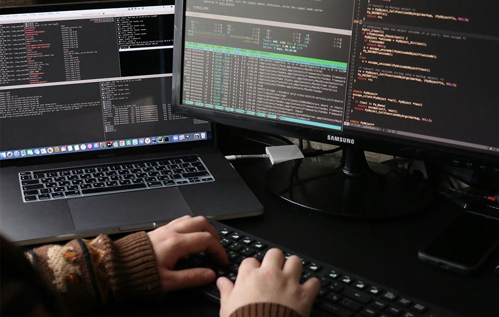 Photograph of a person coding with a dual monitor setup.