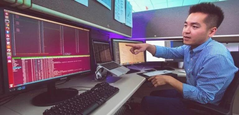 System coder pointing at a computer screen at his desk.