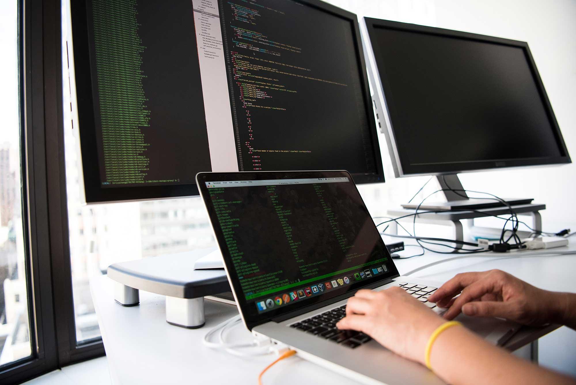 A work desk with multiple screens, each displaying a code editor, as a person types