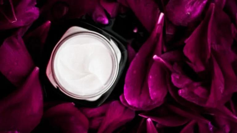 Image of an open jar of skincare lotion with rose pedals surrounding the jar.