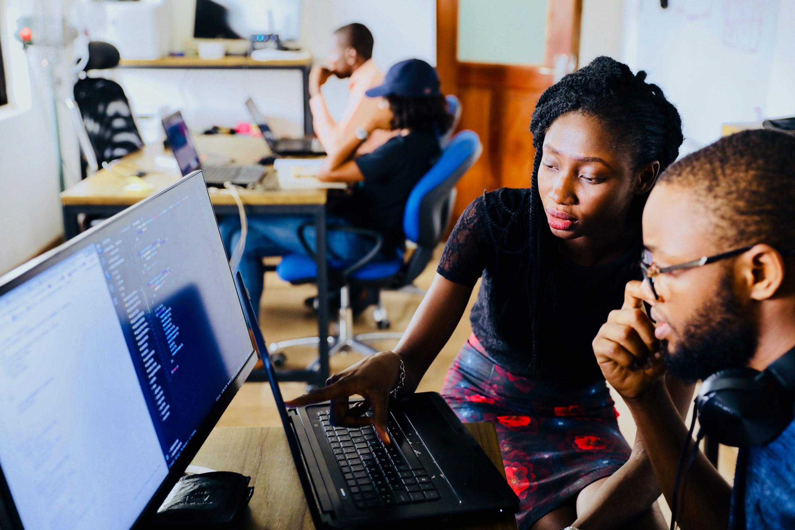 Two people looking at a computer screen together, with one pointing at a selection of code on the screen
