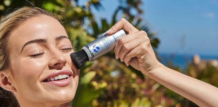Image of woman putting on ISC sunscreen product under the sun with a smile.